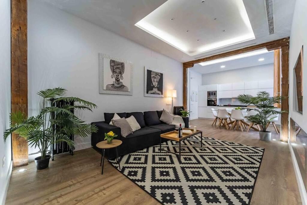 A modern living room with a black sofa, a patterned rug, and a dining area with chairs.