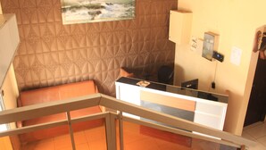 A reception area with a cushioned bench, a reception desk, a wall-mounted air conditioner, and a painting of a seascape. - Hotel Exelle-Xior (Yaoundé)