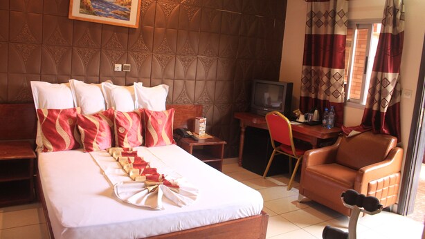 A hotel room with a bed, a desk with a television, a leather armchair, and a window with curtains. - Hotel Exelle-Xior (Yaoundé)