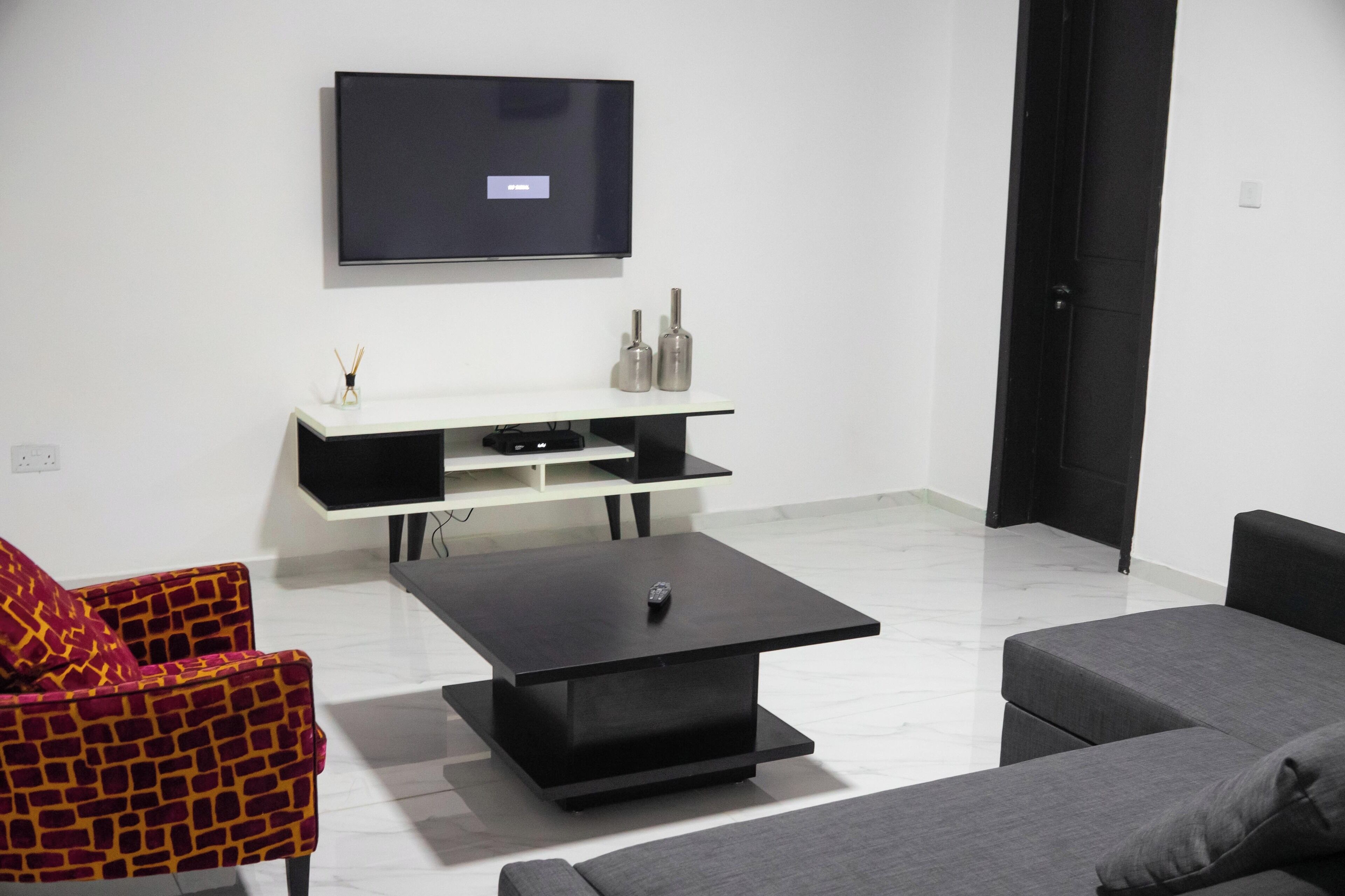 Ein modernes Wohnzimmer mit einem flachbildfernseher an der Wand, einem schwarzen Couchtisch, einem grauen Sofa und einem gemusterten Sessel.