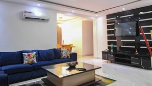 Una sala moderna con un sofá azul, una mesa de centro de vidrio y un televisor sobre un mueble negro.