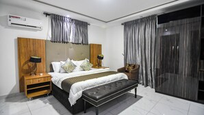 Un dormitorio moderno con una cama grande, un banco, una mesita de noche, un aire acondicionado y una puerta corrediza de cristal.