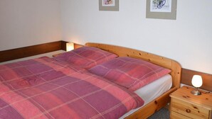 A bed with a plaid blanket and pillows, a wooden nightstand with a lamp, and framed pictures on the wall. - Nice apartment for rent in les Collons (Thyon-Les Collons)