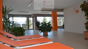 A spacious indoor area with orange lounge chairs, potted plants, and a sign reading "thyon Immobilier". - Nice apartment for rent in les Collons (Thyon-Les Collons)