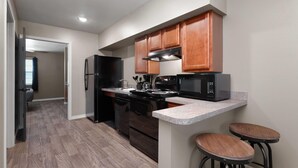 Una cocina moderna con armarios de madera, un refrigerador negro, una estufa y un microondas. Hay una encimera con dos taburetes.