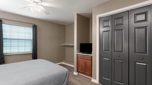 Un dormitorio con cama, ventilador de techo, televisor y armario.