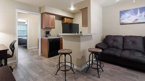 Un espacio habitable compacto con kitchenette, un sofá de cuero oscuro y dos taburetes.