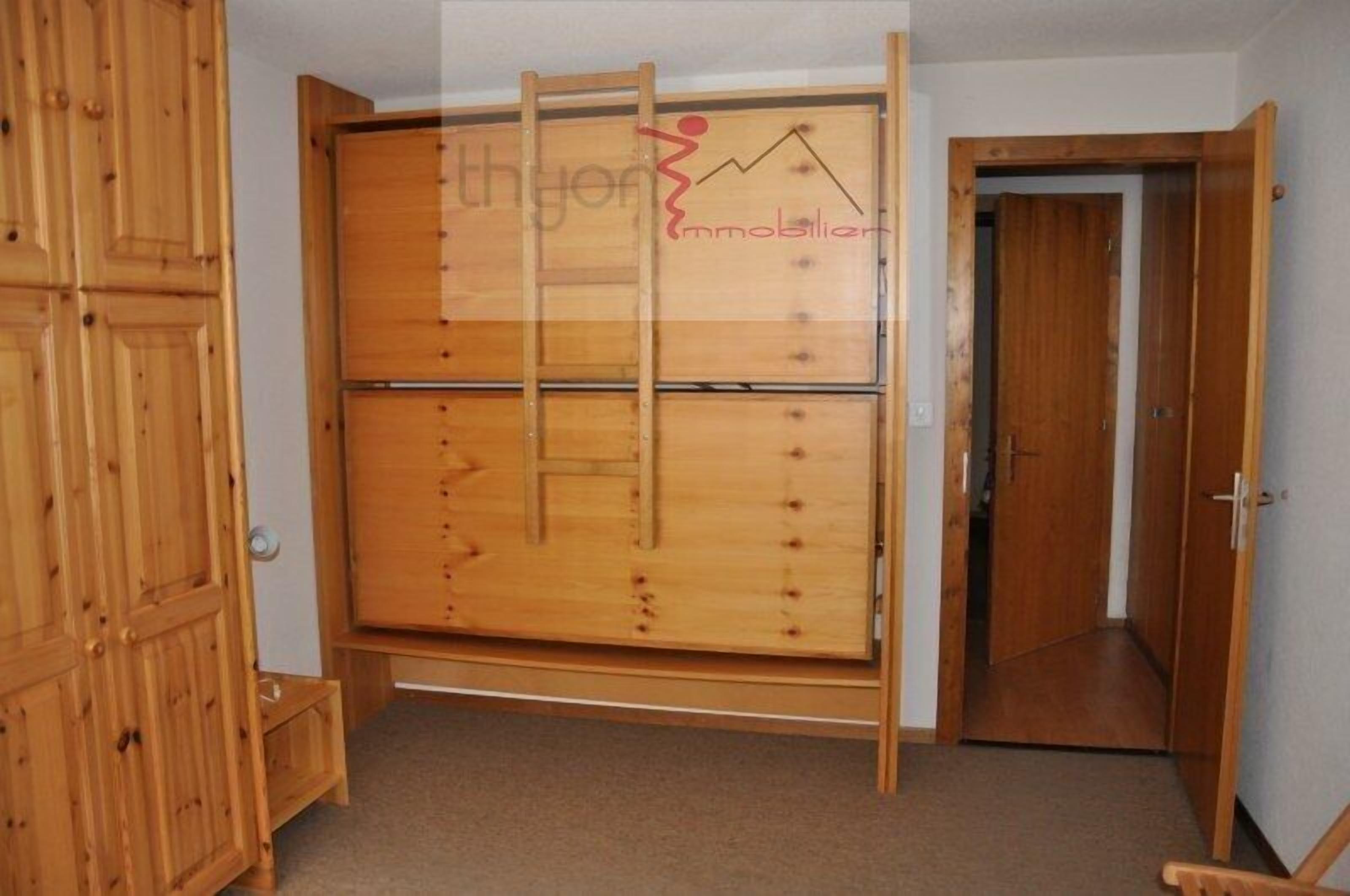 A room with a wooden wardrobe, a door, and a carpeted floor.