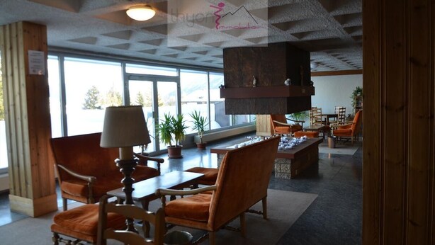 A spacious lobby with wooden furniture, a fireplace, and large windows offering a view of the outdoors. - Nice renoveted flat for rent in Les Collons (Thyon-Les Collons)