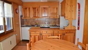 A wooden kitchen with a dining table and chairs, wooden cabinets, a clock, and a ski rack. - Nice renoveted flat for rent in Les Collons (Thyon-Les Collons)