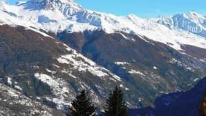 Eine gebirgige Landschaft mit schneebedeckten Gipfeln und dem Logo von 'Thyon Immobilier' am Himmel.