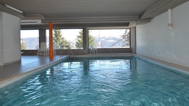 Una piscina interior con agua azul cristalina, una escalera y vistas a montañas a través de amplios ventanales.