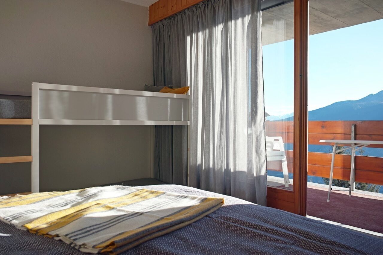 Une chambre avec un lit superposé, une fenêtre avec des rideaux et une vue sur les montagnes.