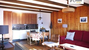 A cozy living room with a red sofa, a wooden dining table with chairs, a kitchen area with wooden cabinets, and a hanging light fixture. - Apartment for rent in les Collons (Thyon-Les Collons)