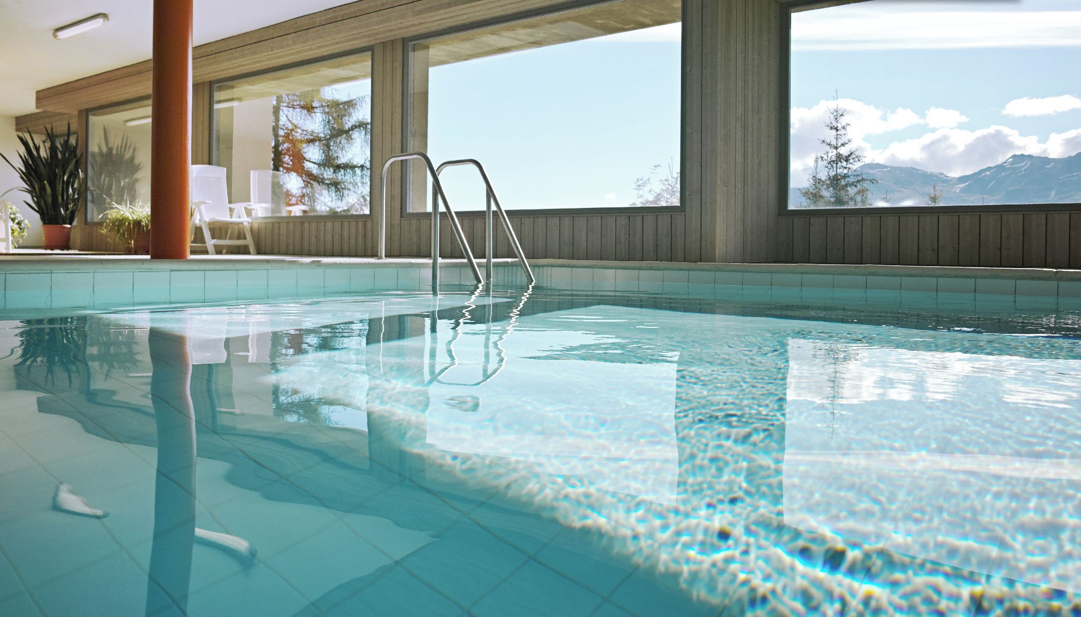 Une piscine intérieure à l’eau claire, dotée d’un plafond en bois et de grandes fenêtres offrant une vue sur les montagnes.