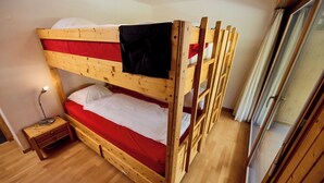 A bunk bed with a wooden frame, a small bedside table, and a window with curtains. - Apartment for rent in les Collons (Thyon-Les Collons)