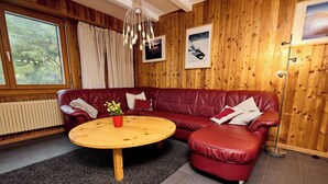 A cozy room with a red leather sofa, a wooden coffee table, and a large window with curtains. - Apartment for rent in les Collons (Thyon-Les Collons)