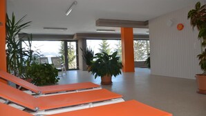 A spacious indoor area with orange lounge chairs, potted plants, and large windows allowing natural light. - Apartment for rent in les Collons (Thyon-Les Collons)