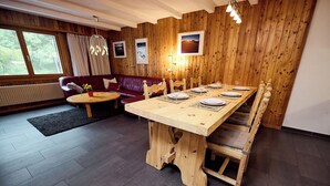 A dining area with a wooden table set for four, a red sofa, and a wooden wall with pictures. - Apartment for rent in les Collons (Thyon-Les Collons)