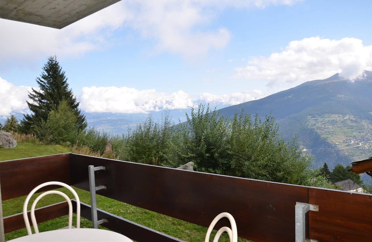 Una terraza con mesa y sillas, con vista a un paisaje montañoso y cielo despejado.
