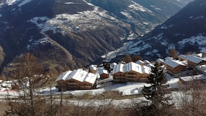 A mountainous landscape with snow-covered peaks and a village with wooden buildings.