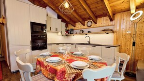 A modern kitchen with white cabinetry, a built-in oven, and a dining area set for six with white chairs and a table set with plates and glasses.
