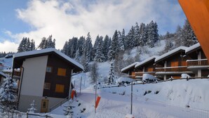 A snow-covered lodge with wooden cabins, a ski slope, and a forested mountain backdrop.