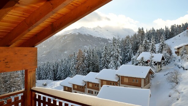 A wooden balcony overlooking a snowy mountain landscape with snow-covered houses.