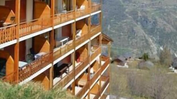 Un edificio de madera de varios pisos con balcones, con montañas al fondo.