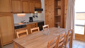 Una cocina de madera con una mesa y sillas, una cafetera y una ventana con cortinas.