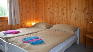 Una cama doble con ropa de cama y almohadas color beige, una ventana con cortina y una pared de madera.