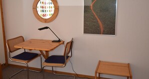 Une pièce avec une fenêtre ronde, une table avec deux chaises, un lampadaire et un tableau encadré au mur.