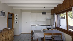 A compact kitchen with white cabinets, a dining table with checkered tablecloth, and a window with curtains. - Beautiful renovated apartment for rent in les Collons (Thyon-Les Collons)