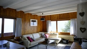 A cozy room with a wooden interior, a white sofa, a coffee table, and large windows. - Beautiful renovated apartment for rent in les Collons (Thyon-Les Collons)