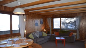 A cozy living room with wooden walls, a round dining table set for four, and two sofas.