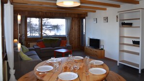 A dining area with a wooden table set for six, a sofa, a television, and a bookshelf.
