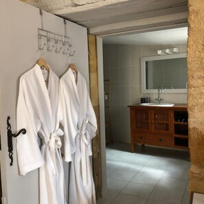 A bathroom with two white bathrobes hanging on a rack, a wooden vanity with a mirror, and a tiled floor. - Le Domaine Aubazen (La Chapelle-Aubareil)