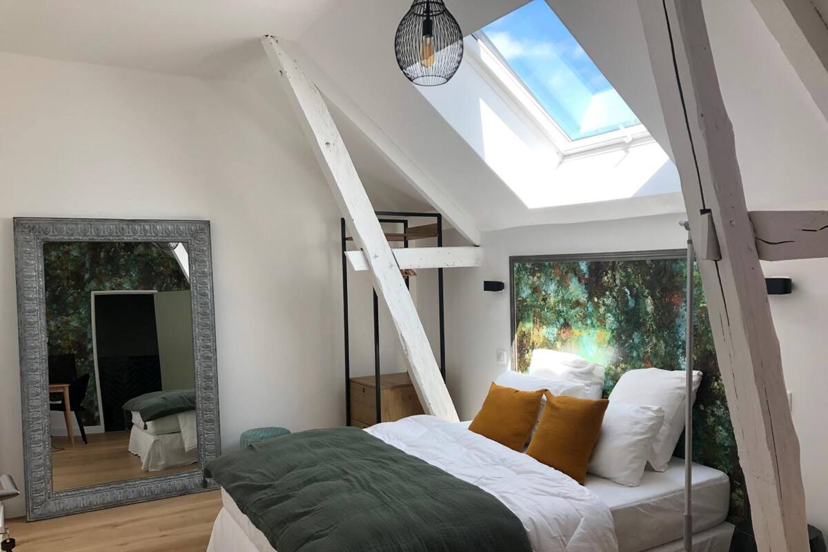 Ein Schlafzimmer mit einer Dachfenster, einem großen Spiegel und einem Bett mit weißer und grüner Bettwäsche.