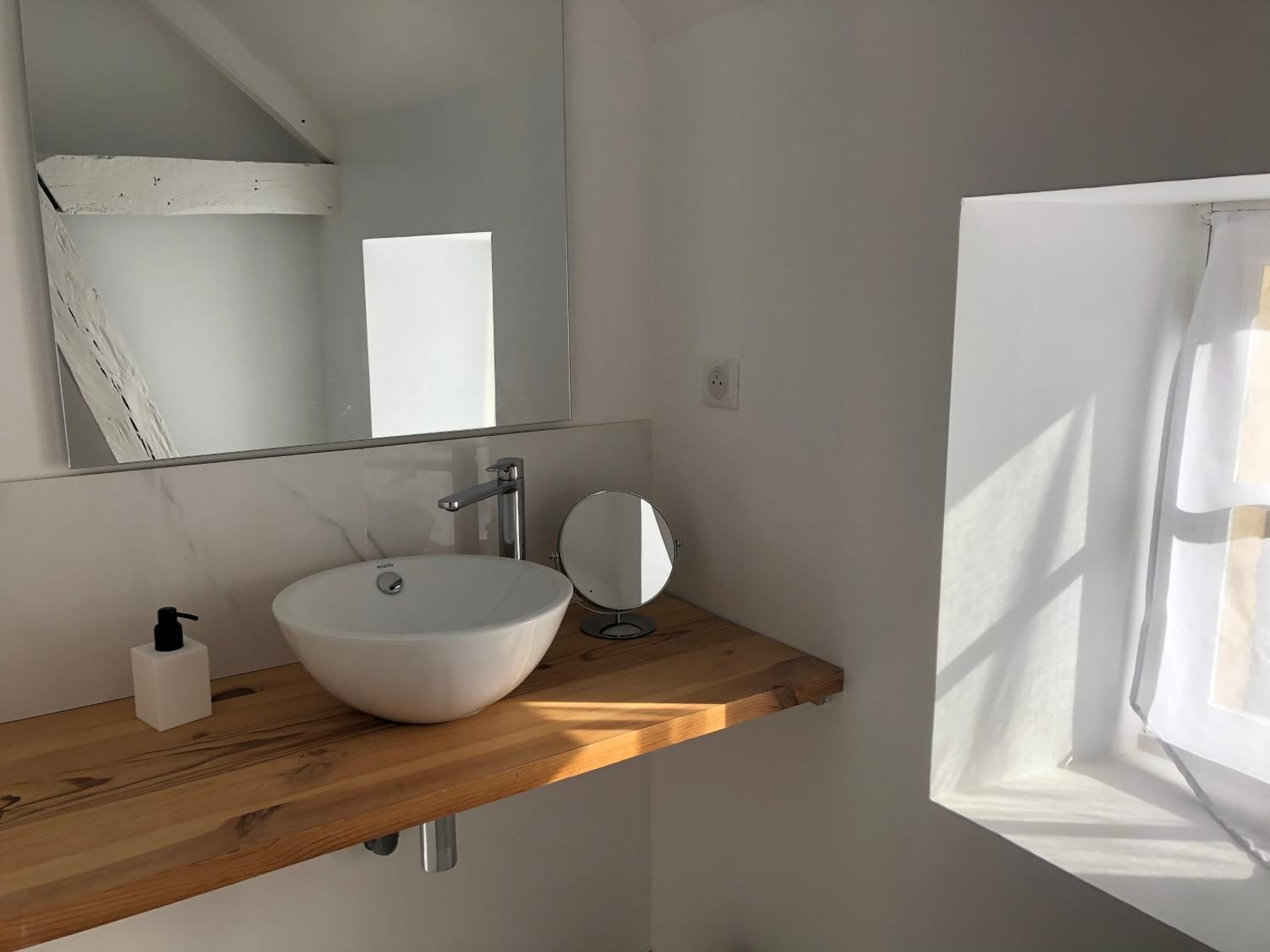 A bathroom with a white sink, a mirror, and a wooden shelf.