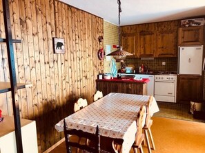 Eine Küche mit Holzausstattung, einem Esstisch mit Stühlen, einer Pendelleuchte und einem Kühlschrank.