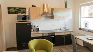 A compact kitchen with a microwave, coffee maker, and a stove. There is a sink with a faucet, and a window with a view of trees. - Ferienwohnung Anke-Apartement 3 (Heinsberg)