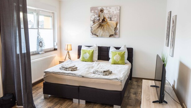 A bedroom with a bed, a bedside lamp, a painting, and a TV. - Ferienwohnung Anke-Apartement 3 (Heinsberg)