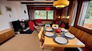 A dining area with a wooden table set for four, a red chair, and a television in the background.
