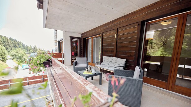 A modern outdoor seating area with a bench, a sofa, and a table, overlooking a scenic hillside.
