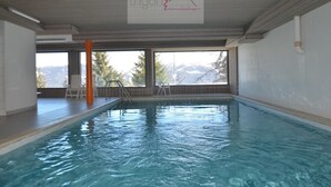 An indoor swimming pool with clear windows, a visible logo, and a view of mountains.