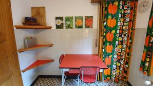 Una piccola cucina con un tavolo e sedie rossi, pavimento piastrellato, mensole in legno e una sveglia a muro.