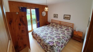 Camera da letto con testiera in legno, copriletto floreale, comodino, tavolo di fianco al letto, uno specchio e vista all'esterno tramite una porta scorrevole.
