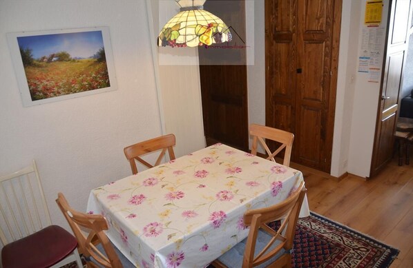 Un comedor con una mesa cubierta por un mantel floral, sillas de madera, una lámpara colgante y un cuadro en la pared.