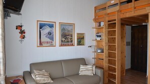 A room with a sofa, a wooden bookshelf, and three framed pictures on the wall. - Nice studio for rent in les Collons (Thyon-Les Collons)