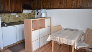 A compact kitchen with wooden cabinets, a tiled backsplash, and a small dining area with a table and chairs. - Nice studio for rent in les Collons (Thyon-Les Collons)